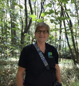 Photo of Kathy KING in the woods in the Appalachian mountains. Woman with light colored hair dark shirt.